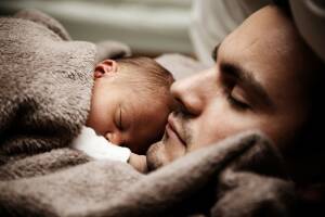 En pyttebebis ligger på sin pappas bröstkorg. Båda sover.