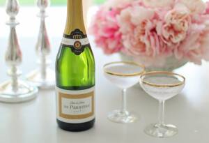 Grön champagneflaska med två gammaldags champagneglas med guldkant. I bakgrunden rosa blommor. Kanske rosor.